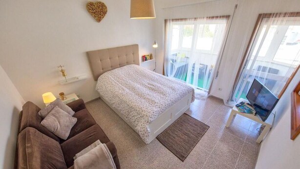 Une chambre à coucher comprenant un lit, un canapé, une télévision et un balcon avec des rideaux.
