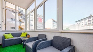 Un balcon doté de meubles en osier, d’un revêtement de sol en gazon synthétique vert et de grandes fenêtres offrant une vue sur les bâtiments.