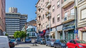 Une vue de rue avec des immeubles à plusieurs étages, des voitures garées et un ciel bleu dégagé.