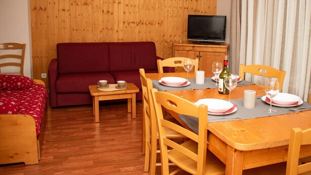 A cozy room with a wooden floor, a red sofa, a dining table with chairs, a small table with cups, and a television on a wooden cabinet. - Duplex chalet 4 rooms, 8 pers, pets allowed, Superdevoluy (Le Dévoluy)