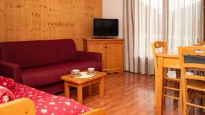 A room with a wooden panel wall, a red sofa, a wooden table with two cups, a television on a wooden cabinet, and a dining table with chairs. - Duplex chalet 4 rooms, 8 pers, pets allowed, Superdevoluy (Le Dévoluy)