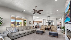 A spacious living room with a grey sofa, ottoman, and patterned armchairs, a ceiling fan, and a fireplace. - Paradise Village 115, Poolside Heaven, has a Private Hot Tub, and View of Lazy River (Santa Clara)