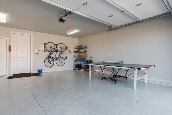 Espaço amplo em ambiente interno com mesa de pingue-pongue, bicicletas e extintor de incêndio.