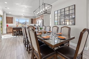 A dining area with a glass table, wooden chairs, and a modern chandelier. - Paradise Village 115, Poolside Heaven, has a Private Hot Tub, and View of Lazy River (Santa Clara)