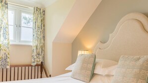 Une chambre avec un plafond en pente, un lit recouvert d’une literie blanche, deux oreillers ornés de motifs représentant des hiboux et une fenêtre agrémentée de rideaux à motifs floraux.