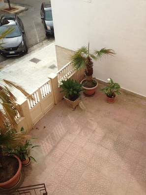 A balcony with potted plants, a tiled floor, and a white wall.