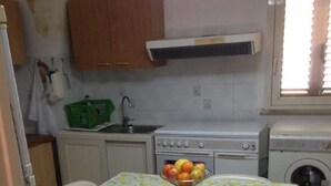 Une cuisine avec une table dressée pour deux personnes, un saladier rempli de fruits et les appareils électroménagers de base.