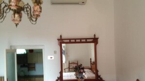 Une chambre avec une commode en bois, un lit recouvert d’une couvre-lit rose, un lustre et un miroir au-dessus de la commode.