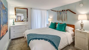Ein Schlafzimmer mit einem Bett, zwei Nachttischen, einer Kommode, einem Spiegel und einem Wandventilator.