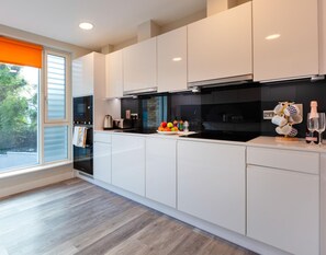 A modern kitchen with white cabinets, a black countertop, and a window with an orange blind. - The Westwood (Galway)