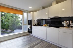 A modern kitchen with white cabinets, a black stove, and a view of trees through a large window. - The Westwood (Galway)