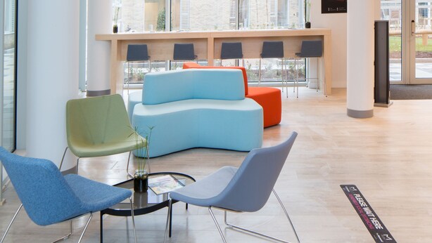 A spacious lobby with a modern blue sofa, green and blue chairs, and a unique hanging light fixture.