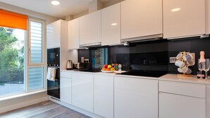 A modern kitchen with white cabinets, a black stove, and a window with an orange blind.