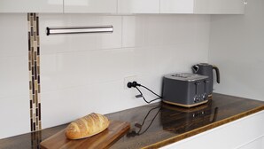 Uma cozinha com bancada de madeira, torradeira, pão numa tábua de corte e painel de azulejos.