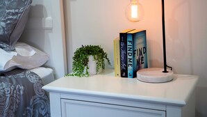Uma mesa de cabeceira com uma luminária, um vaso de planta e uma pilha de livros.