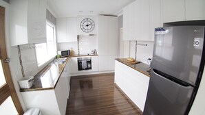 Uma cozinha moderna com armários brancos, geladeira de aço inoxidável, micro-ondas e um relógio na parede.
