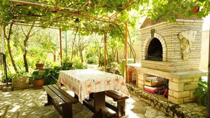 Une terrasse extérieure avec une table en pierre, des bancs et un four en briques.