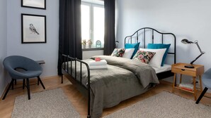 Un dormitorio con una cama, una silla, una mesita de noche y dos cuadros en la pared.
