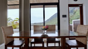Un coin repas avec une table en verre, des chaises en osier et une vue sur un paysage montagneux.