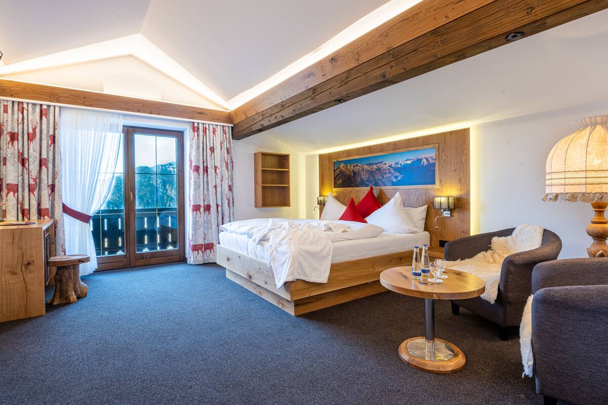 Ein Schlafzimmer mit Bett, einer Couch, einem kleinen Tisch und einem Balkon mit Vorhängen.