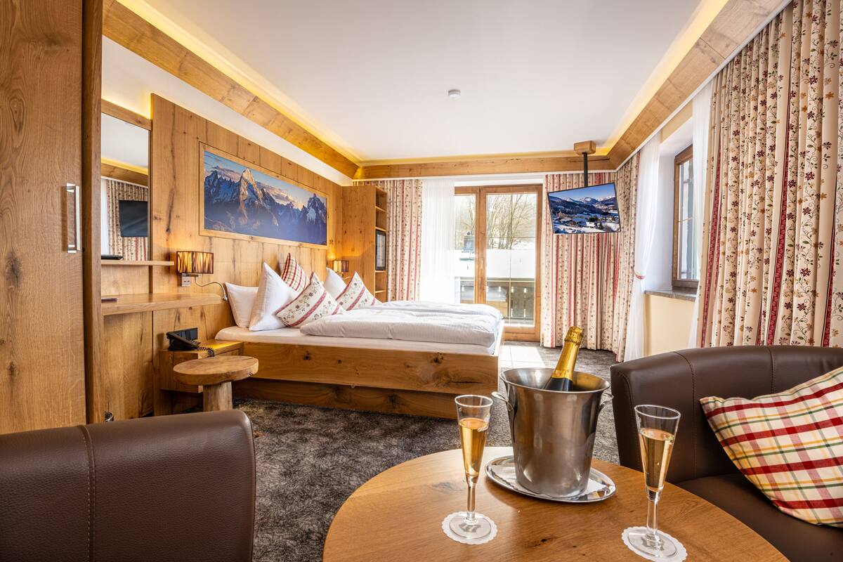 Ein gemütliches Hotelzimmer mit einem hölzernen Bett, einem Fernseher, einem Balkon und zwei Sektgläsern auf einem Tisch.