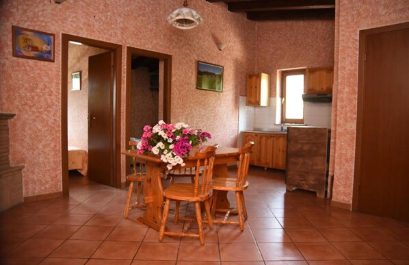 A dining area with a wooden table and chairs, a floral centerpiece, and a kitchen in the background.