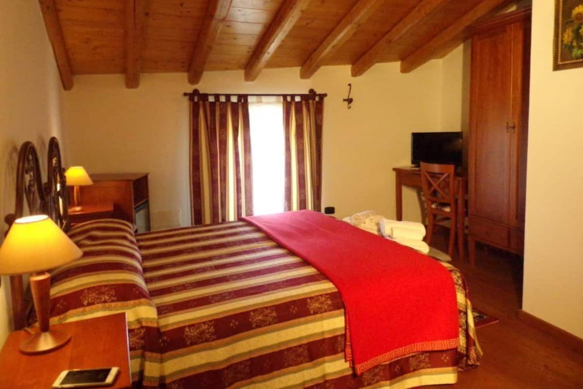 Ett hotellrum med ett träpanelat tak, en säng med randigt sänglinne, en röd pläd, en sänglampa, en tv och en trägarderob.