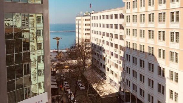 A multi-story building with a parking lot in front, a clear view of the sea, and a sign for 'IZIKA'.