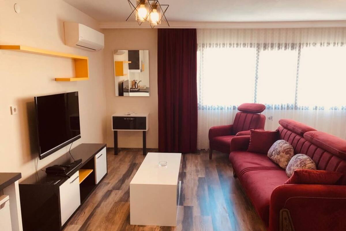 A modern living room with a flat-screen TV, a white coffee table, a red sofa, and a wooden floor.
