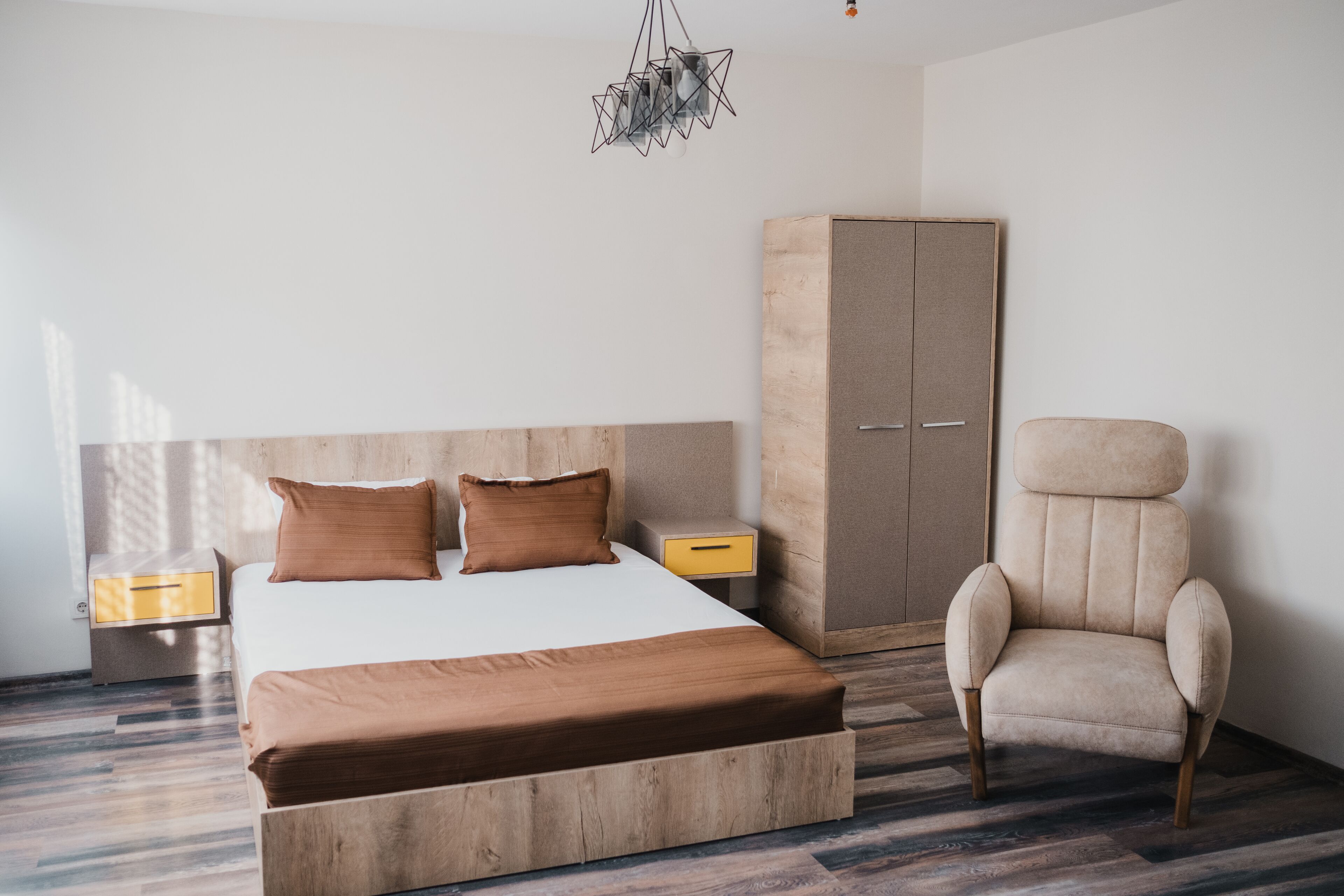 A bedroom with a large bed, wooden headboard, a wardrobe, a chair, and a nightstand with a lamp.