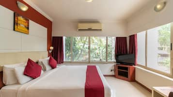 A hotel room with a large bed, a flat-screen TV, and a window with a view of greenery.