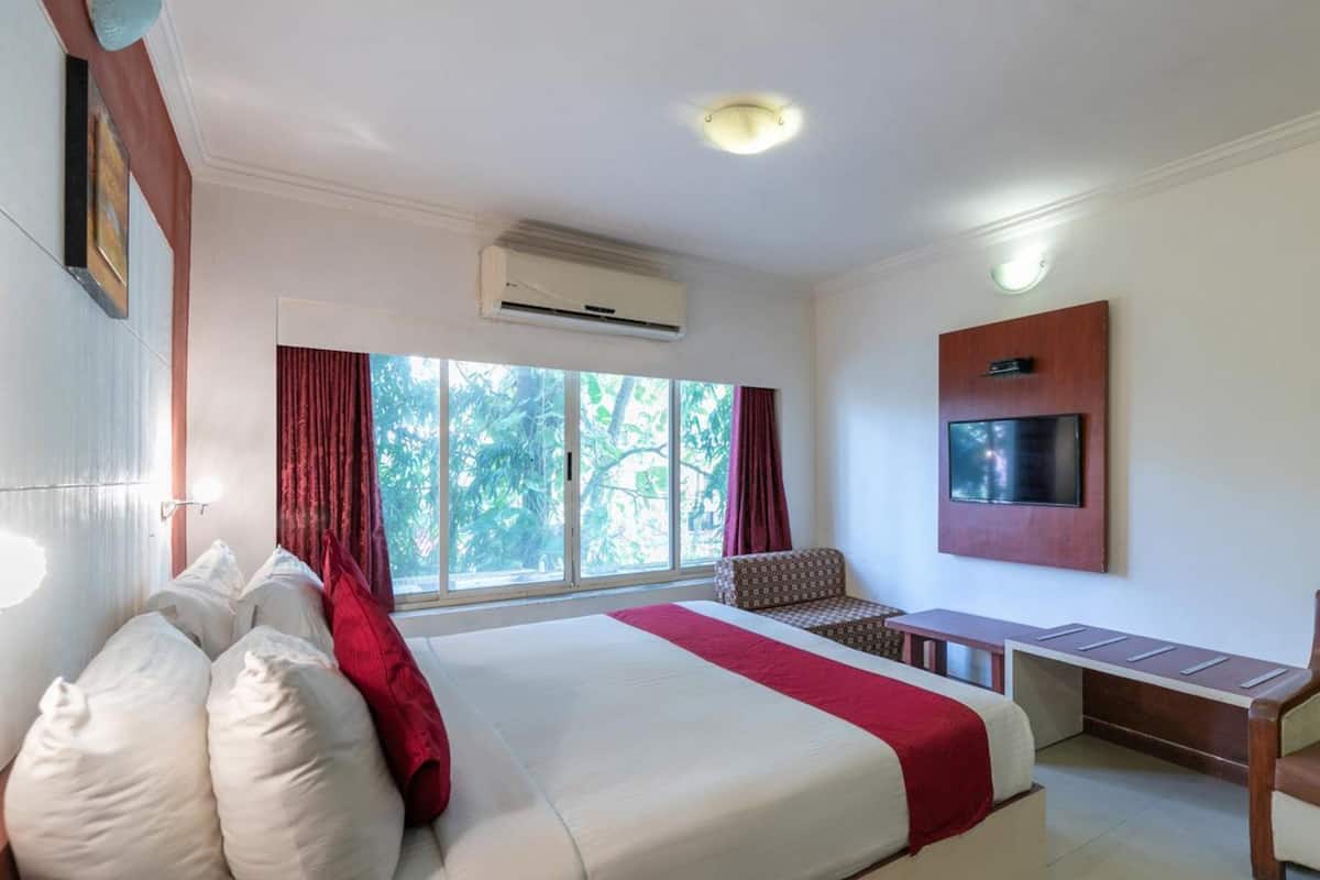 A hotel room with a large bed, a desk, a chair, and a TV mounted on the wall.