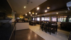 Um restaurante amplo com várias mesas e cadeiras, um balcão e janelas grandes que oferecem vista para o exterior.