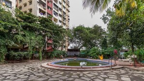 Um pátio com uma piscina circular, rodeado por um chão de ladrilhos de pedra e vegetação exuberante.