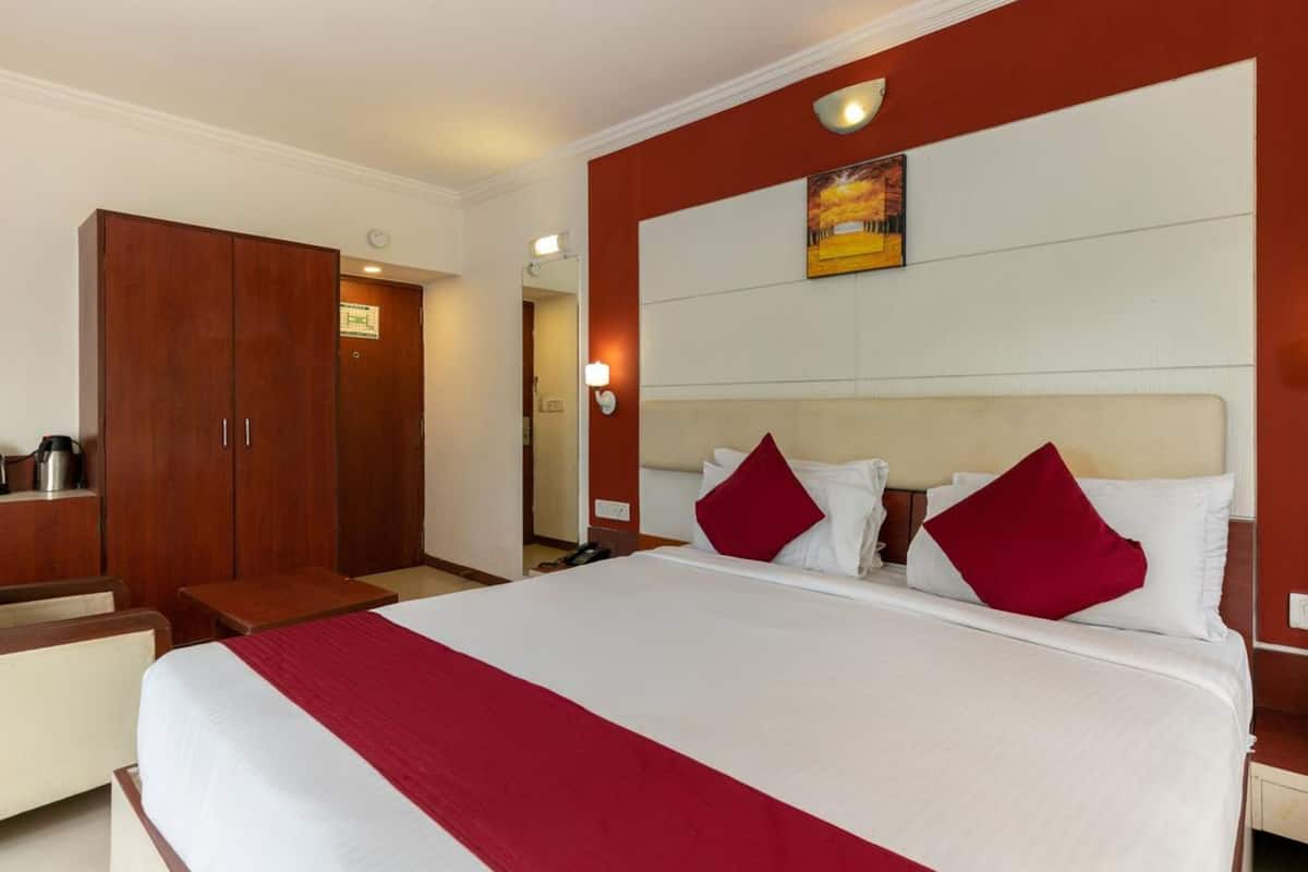 A hotel room with a large bed, a wooden wardrobe, a desk, and a nightstand.