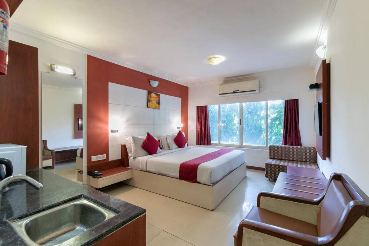 A hotel room with a bed, a sofa, a small table, a sink, and a window with curtains.