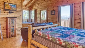 A log cabin bedroom with a wooden bed, a ceiling fan, and a large window overlooking a snowy landscape. - All About The View, Spacious Mountain Getaway, Perfect for Families & Groups (Sevierville)