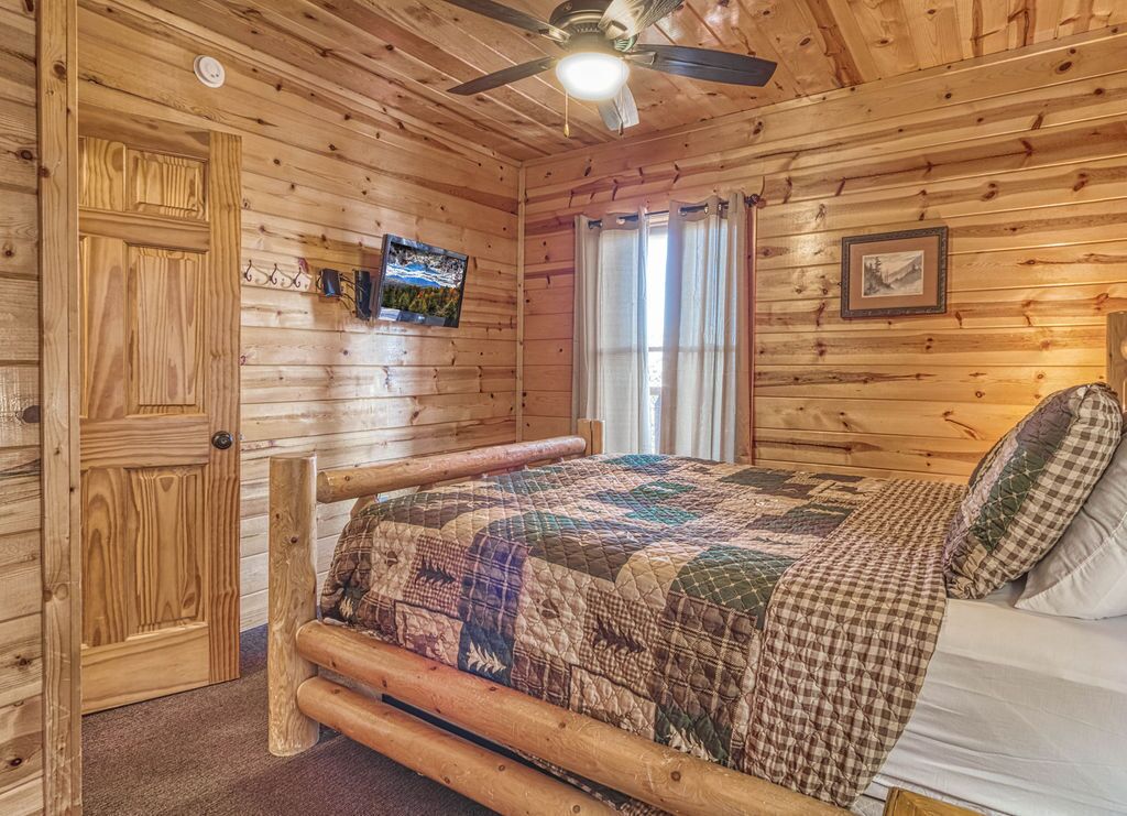 A wooden cabin room with a bed, a ceiling fan, and a door.