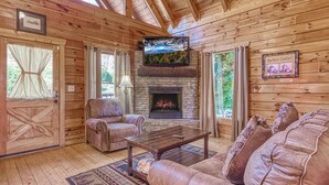 A log cabin interior with leather sofas, a fireplace, and a television mounted above it. - All About The View, Spacious Mountain Getaway, Perfect for Families & Groups (Sevierville)