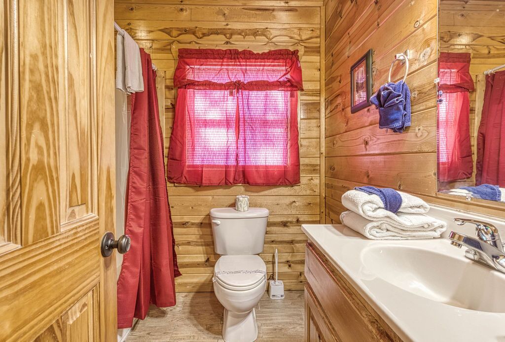 Een houten badkamer in een hutje, met toilet, wastafel en rode gordijnen.