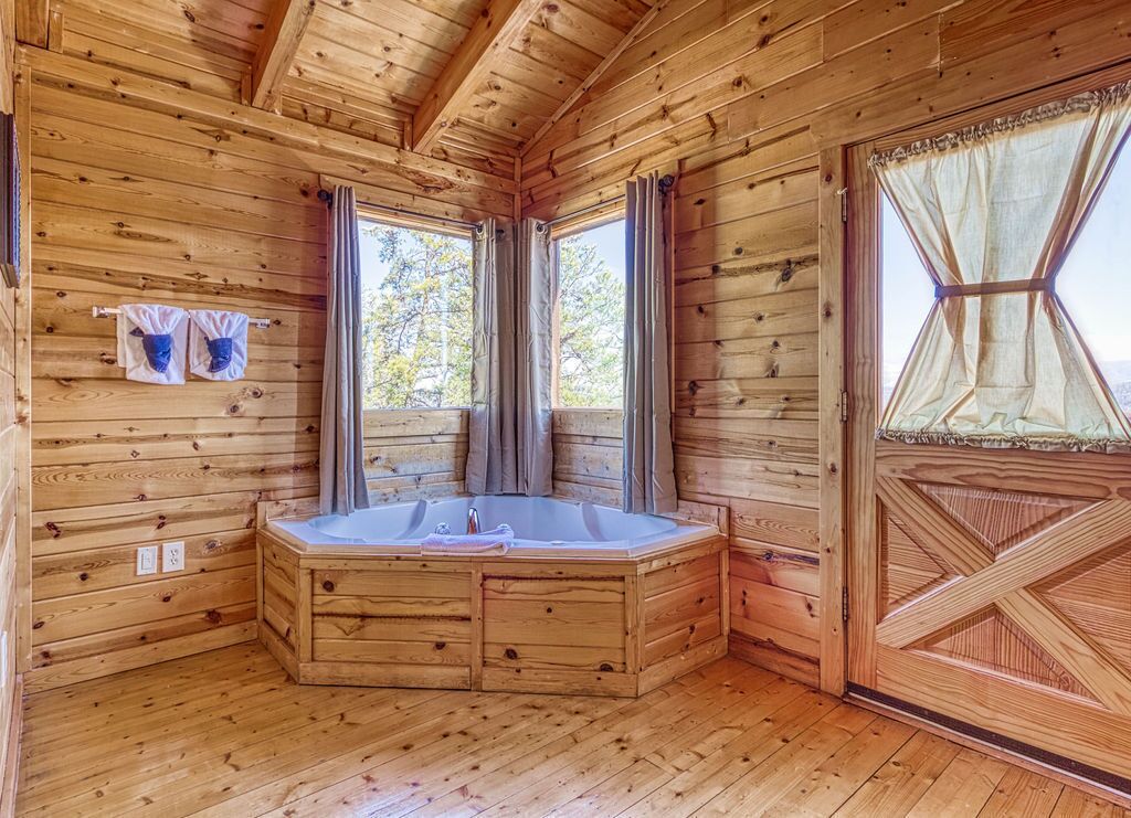 A wooden cabin with a corner bathtub, large windows, and a door with a decorative pattern.