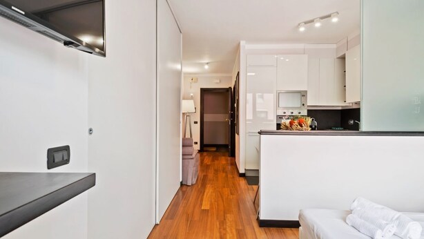 Una habitación de hotel moderna con suelo de madera, una cama, kitchenette y un pasillo que conduce a otra habitación.