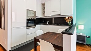 Una cocina moderna con armarios blancos, una mesa de comedor de madera y una mesita auxiliar con una lámpara.