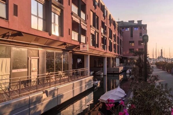 A multi-story building with balconies, a covered walkway, and a view of a canal.