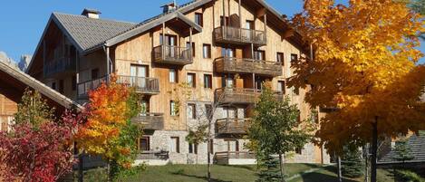 A multi-story wooden building with balconies, surrounded by autumn foliage.