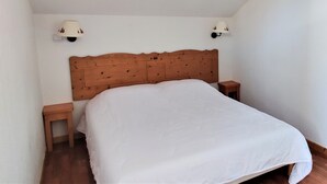 A bedroom with a wooden headboard, two bedside tables, and a white bedspread. - Charming 3-room chalet for 6 guests in Superdevoluy (Le Dévoluy)