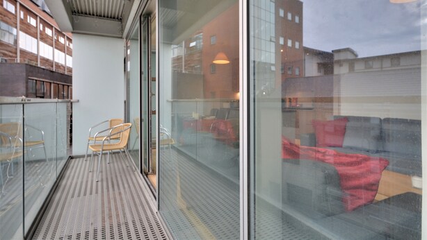 Un balcon doté d’une porte vitrée, d’une chaise en métal et offrant une vue sur un immeuble avec de nombreuses fenêtres.
