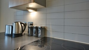 Une cuisine dotée d’un plan de travail noir, d’appareils électroménagers en acier inoxydable et de murs recouverts de carreaux gris.