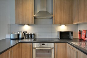 A modern kitchen with wooden cabinets, a stainless steel range hood, a microwave, a kettle, and a toaster. - Cheapside by Top House (Liverpool)