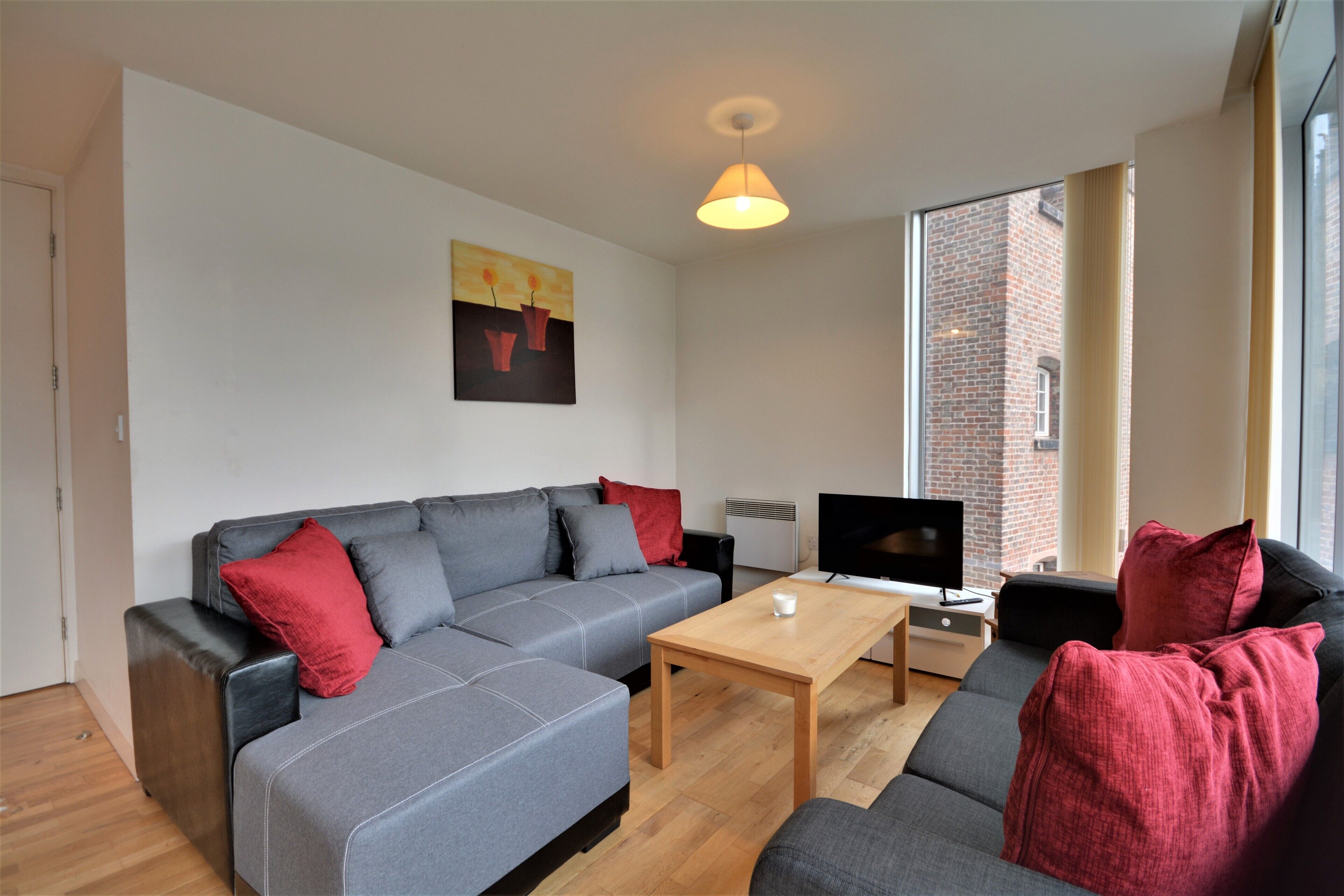 A modern living room with a grey sofa, red cushions, a wooden coffee table, and a flat-screen TV.
